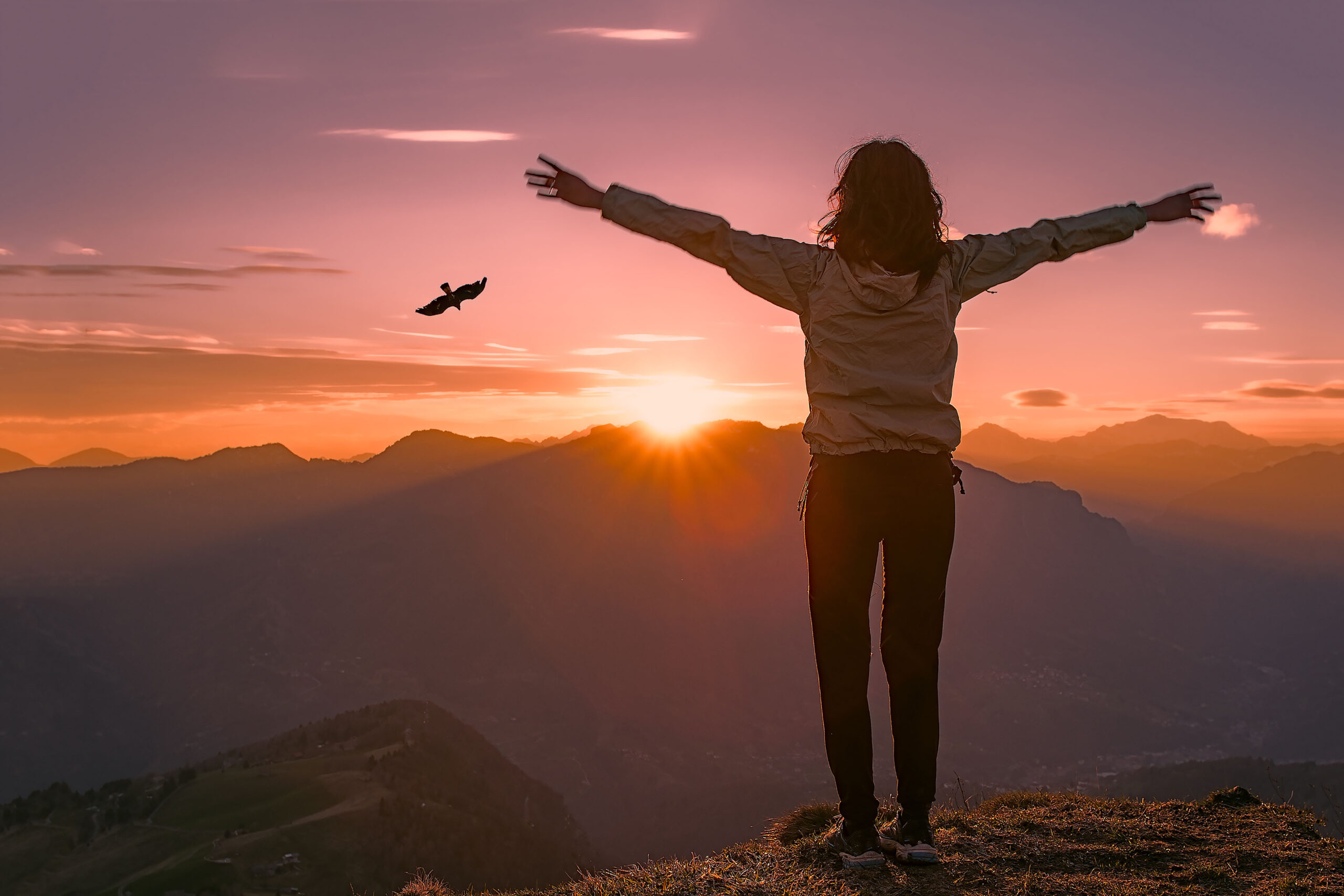 Woman on top of a mountain at sunset looks eagle and open arms
